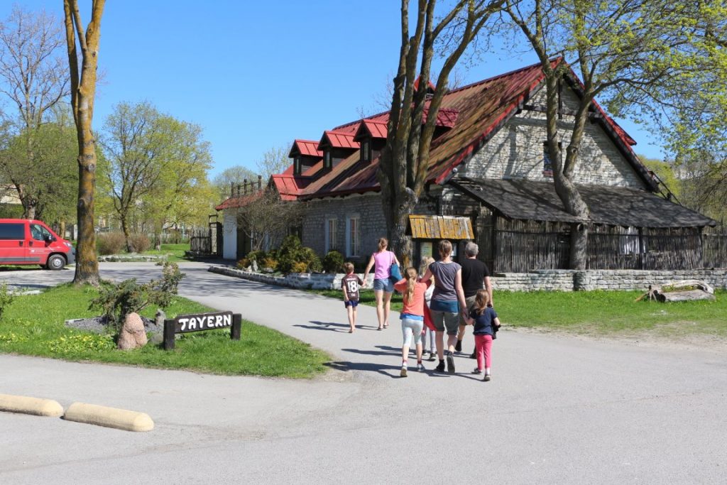 Auf dem Bild sieht man zwei Familien, die gerade die Einfahrt zur Taverne "Peetri Toll" betreten. Das Restauran ist ein älteres, aus Naturstein gebautes Gebäude mit rotem Ziegeldach.